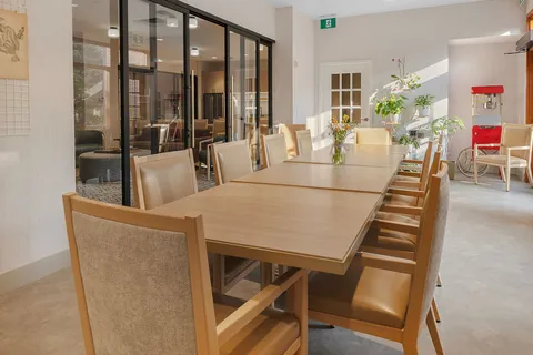 Long dining table beside glass walls and wooden chairs.