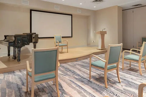 Theatre room with a piano, projection screen and blue chairs.