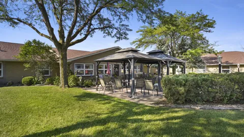 Lawn and patio with chairs beneath a dark-roofed gazebo beside the residence