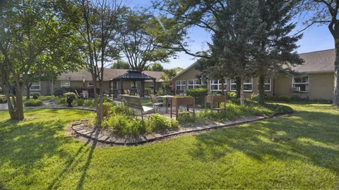 Single-storey building surrounding a garden with raised beds, trees and a gazebo