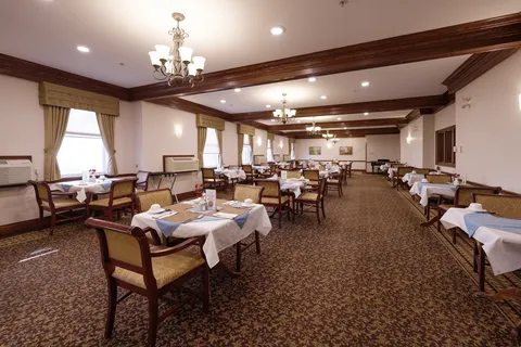 Dining room with set tables, wooden chairs, chandeliers and dark ceiling beams.