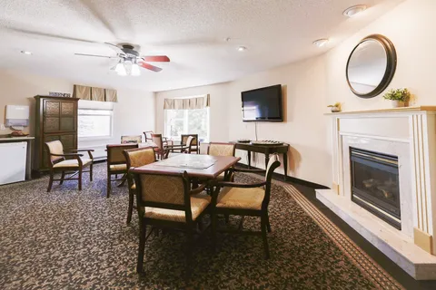 Common room with tables, chairs, a fireplace and a wall-mounted television.