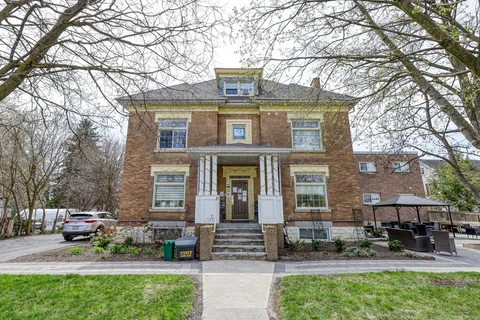 Brick residence with front steps, a porch, lawn and large trees.