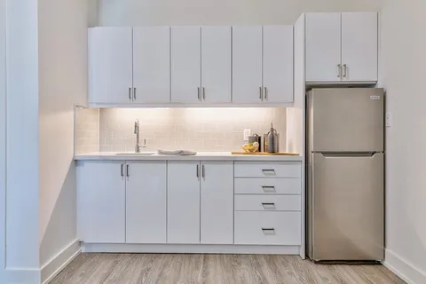 Kitchenette with white cabinets, sink and refrigerator.