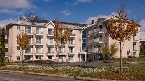 Pale multi-storey residence with balconies and trees beside the street