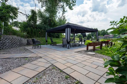 Paved garden patio with a gazebo, outdoor chairs and raised planting beds