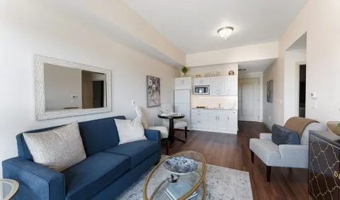 Sitting area with a blue sofa, armchair, tables and a kitchenette