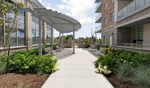 Paved courtyard with benches, plantings and a pergola beside a building