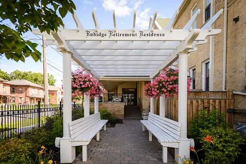 White pergola with benches and hanging flower baskets beside the building