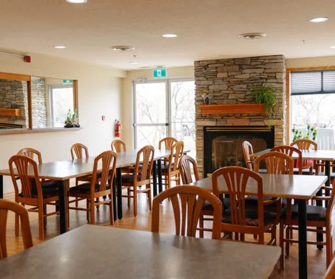 Dining room with wood tables and chairs, windows and a fireplace.