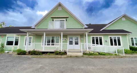 Pale green residence with white railings, covered porches and a paved forecourt