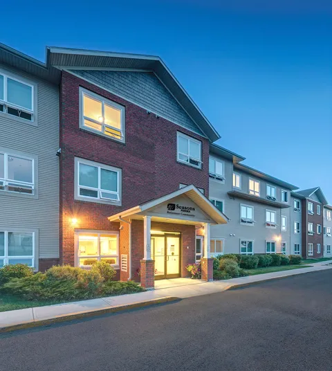 Residential building at dusk with a lit entrance, windows and planted beds
