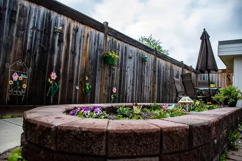 Raised flower bed beside a fenced patio with chairs and an umbrella