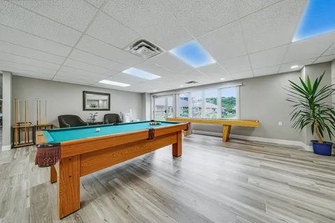 Room with a billiards table and shuffleboard beside large windows