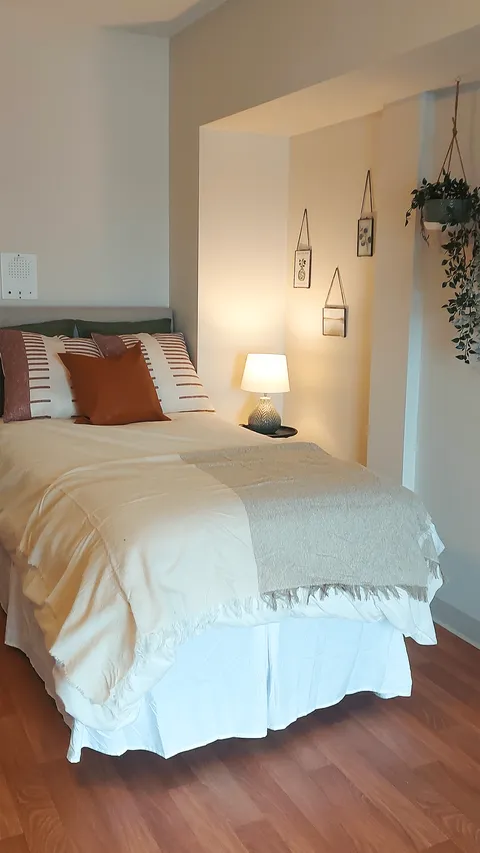 Bedroom with a white bedspread, bedside lamp and hanging botanical decorations.