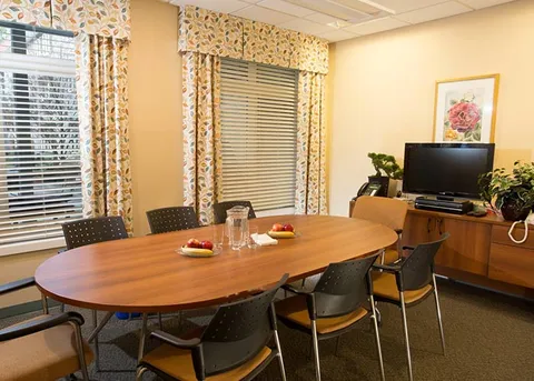 Meeting room with a round table and chairs beside tall windows.