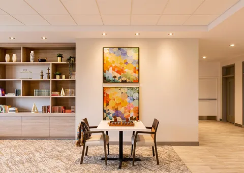 Chess table and chairs beside bookshelves and colourful abstract paintings