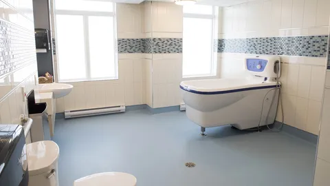 Bright tiled bathroom with an accessible bathtub, sink and large windows