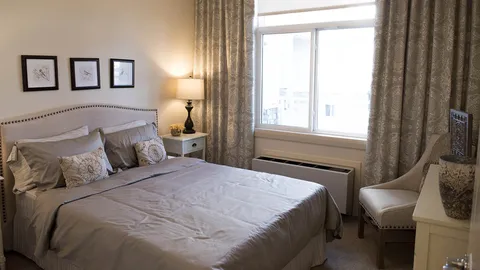 Bedroom with a bed, bedside table and an armchair beside the window