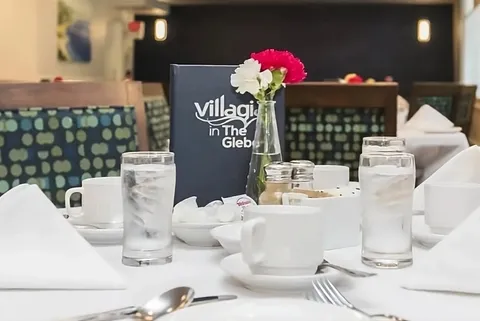 Dining table set with glasses, cups, folded napkins, a menu and a vase of pink and white flowers