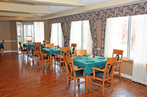 Dining room with green tablecloths and wooden chairs beside large windows