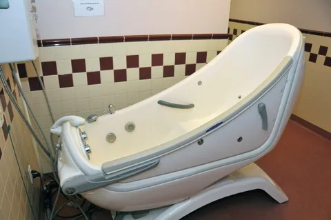 Bathing tub with handrails beside a tiled wall