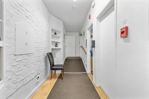 Hallway with a white brick wall, black chair, carpet runners and a wooden handrail
