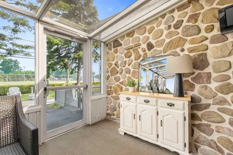 Glass-roofed sunroom with a stone wall, wicker chair, sideboard and mirror