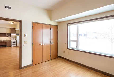 Empty room with a closet, large window and an adjoining kitchenette
