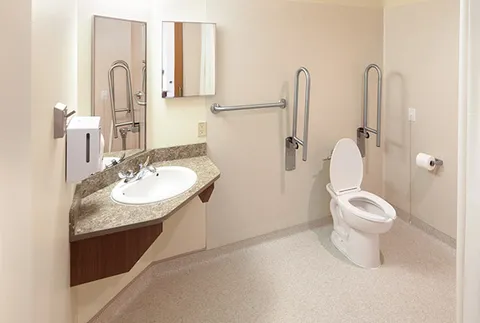 Bathroom with a sink, toilet, mirrors and grab rails