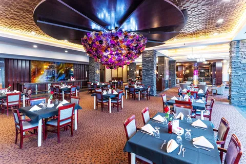 Set dining tables beneath a purple chandelier and patterned ceiling