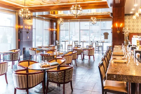 Small dining tables and a bar counter beside large windows