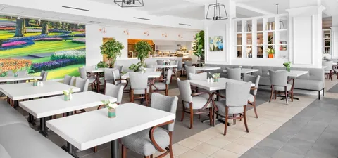 Dining area with square tables, grey chairs and colourful landscape artwork