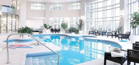 Indoor pool with handrails and seating beside tall glass walls