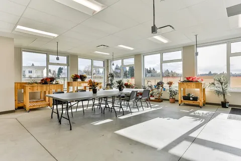 Tables and chairs among plant benches in a bright room with large windows