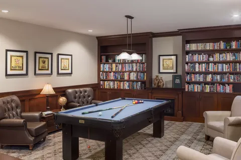 Room with a pool table, armchairs and bookshelves