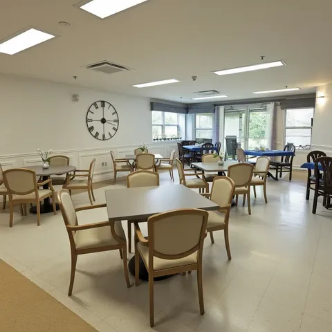 Dining tables with wooden chairs beneath ceiling lights and a wall clock