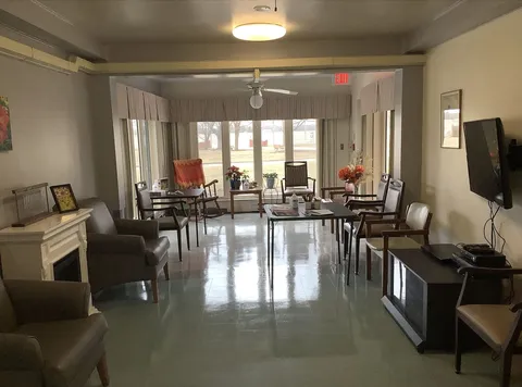 Armchairs and small tables beside a fireplace and large windows
