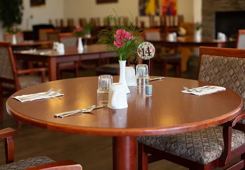Round dining table set with glasses, mugs, cutlery and a small vase of flowers