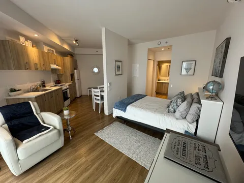 Studio apartment with a bed, sitting chair and kitchenette.