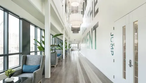Bright corridor with large windows, ceiling lights and a wooden floor.