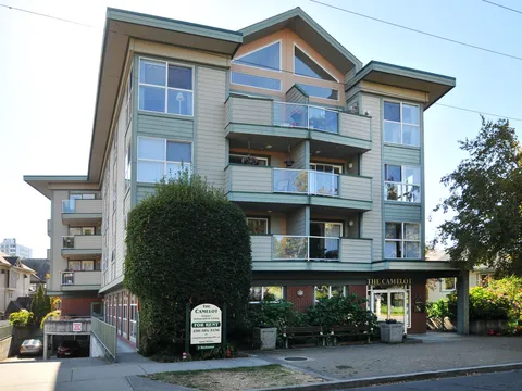 Apartment building frontage with balconies, trees and an entrance.