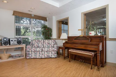 Piano and upholstered seating beside large windows.