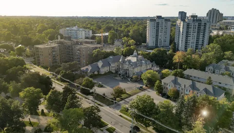Aerial view of a turreted residence and adjacent buildings amid trees