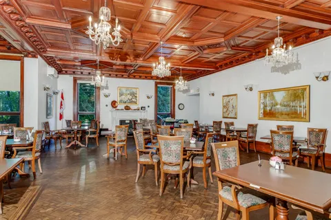 Dining room with wooden tables, floral-upholstered chairs, chandeliers and a coffered wooden ceiling
