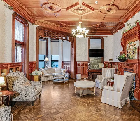 Sitting room with ornate wooden ceiling panels, armchairs, sofas and a fireplace