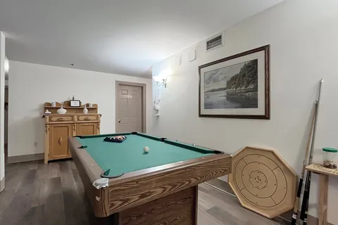 Billiards table beside a wall picture and wooden cabinet.
