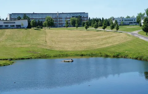 Large building beyond a pond, lawns, trees and a curved paved path
