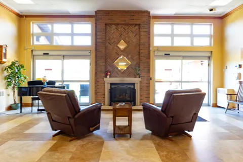 Two brown armchairs facing a brick fireplace between large windows