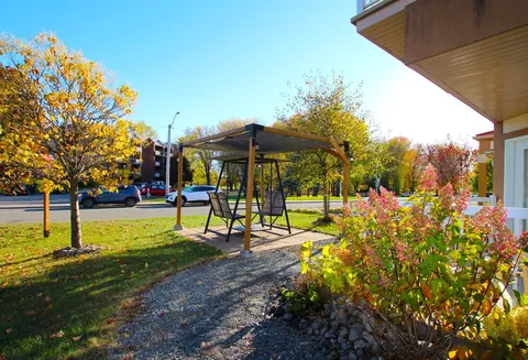 Garden seating area with a covered swing, flowers and trees.